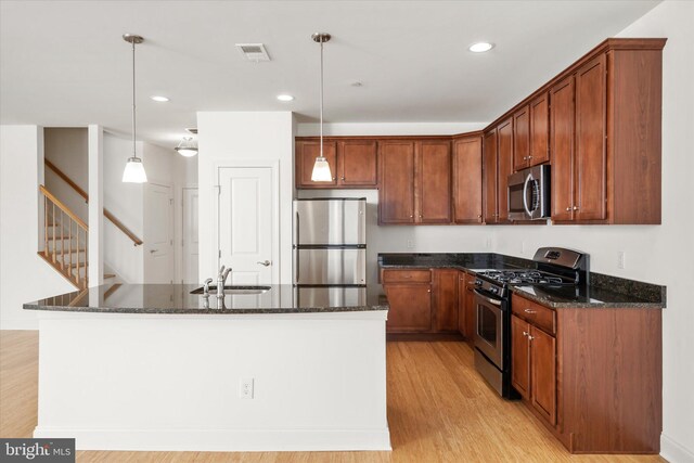 kitchen featuring visible vents, a sink, dark stone counters, appliances with stainless steel finishes, and light wood finished floors