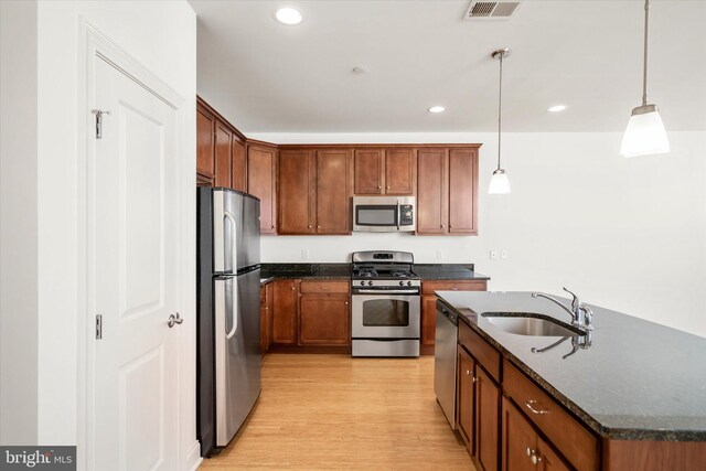 kitchen featuring visible vents, a sink, dark stone counters, appliances with stainless steel finishes, and light wood finished floors