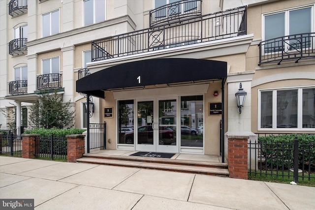 view of exterior entry featuring french doors, stucco siding, and fence