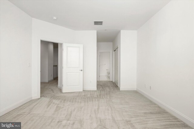 unfurnished bedroom with light colored carpet, baseboards, visible vents, and connected bathroom