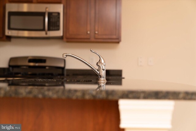 kitchen featuring stainless steel microwave, brown cabinets, and dark countertops