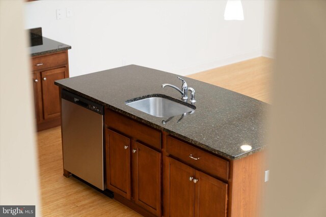 kitchen with a sink, dark stone counters, light wood-type flooring, stainless steel dishwasher, and a kitchen island with sink