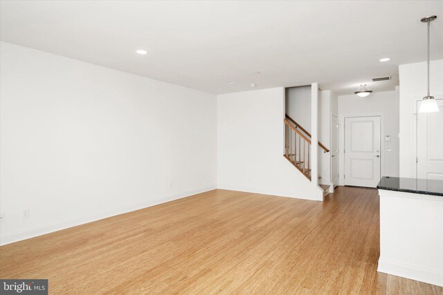 unfurnished living room with light wood finished floors, visible vents, stairs, and baseboards