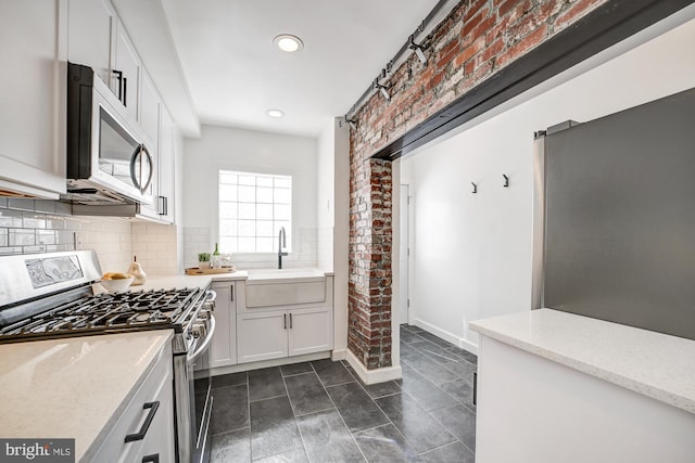 kitchen with sink, white cabinets, stainless steel appliances, backsplash, and brick wall