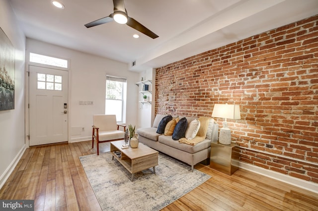 living room with light hardwood / wood-style floors, ceiling fan, and brick wall