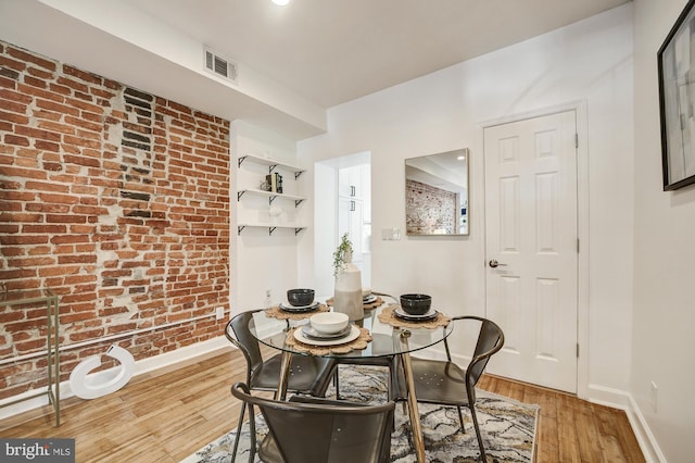 dining room with wood-type flooring and brick wall