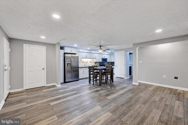 kitchen with appliances with stainless steel finishes, white cabinets, a textured ceiling, light wood-type flooring, and ceiling fan