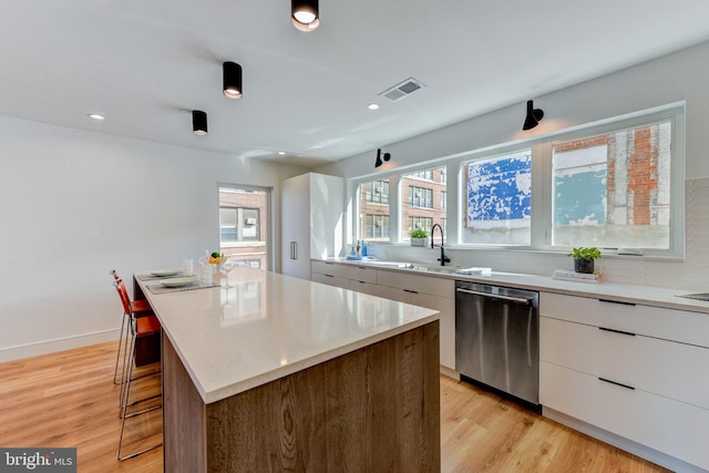 kitchen featuring a center island, white cabinetry, light hardwood / wood-style flooring, and stainless steel dishwasher