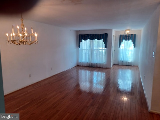 spare room featuring wood-type flooring and an inviting chandelier