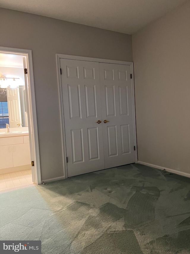 unfurnished bedroom featuring a closet, ensuite bath, carpet, and a sink