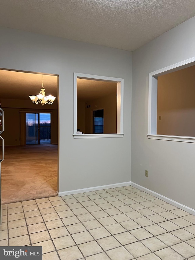 unfurnished room with baseboards, light colored carpet, an inviting chandelier, and a textured ceiling