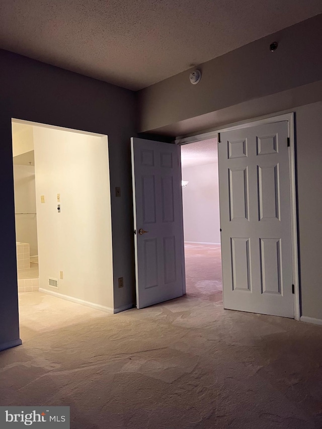 unfurnished bedroom featuring carpet flooring, connected bathroom, a textured ceiling, and visible vents