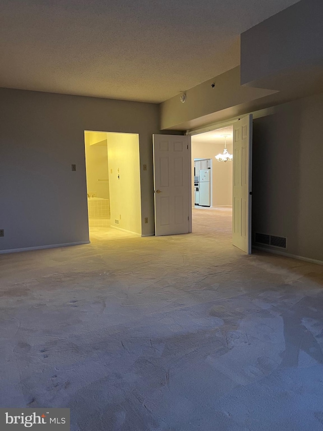 unfurnished room with visible vents, light colored carpet, a textured ceiling, and an inviting chandelier