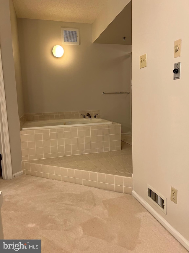 bathroom with visible vents, baseboards, tiled tub, and a textured ceiling