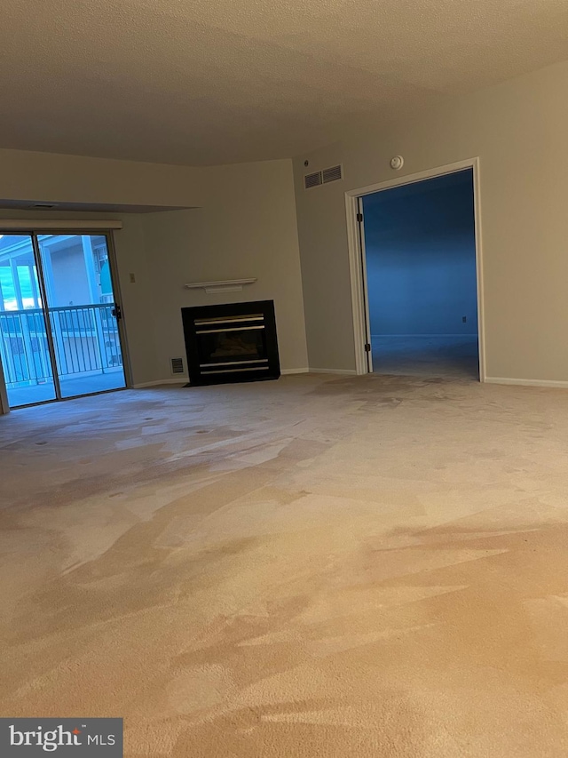 unfurnished living room with a glass covered fireplace, visible vents, carpet floors, and a textured ceiling