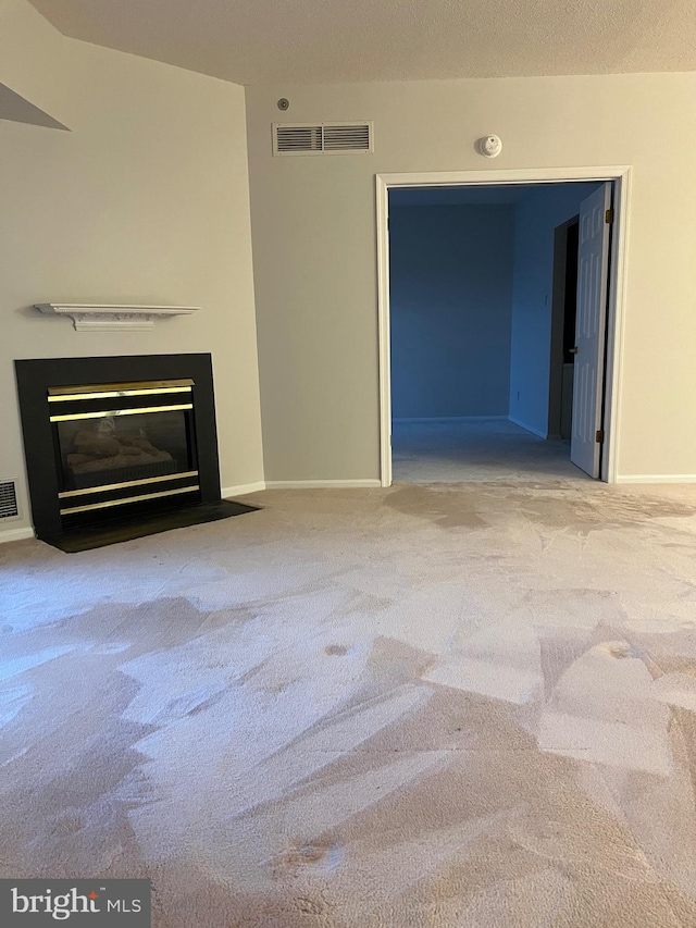 unfurnished living room with visible vents, a fireplace with flush hearth, carpet, and baseboards