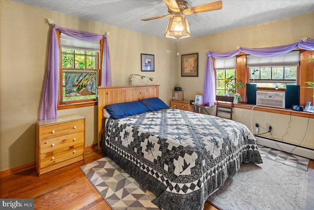 bedroom featuring cooling unit, hardwood / wood-style floors, ceiling fan, and a baseboard radiator