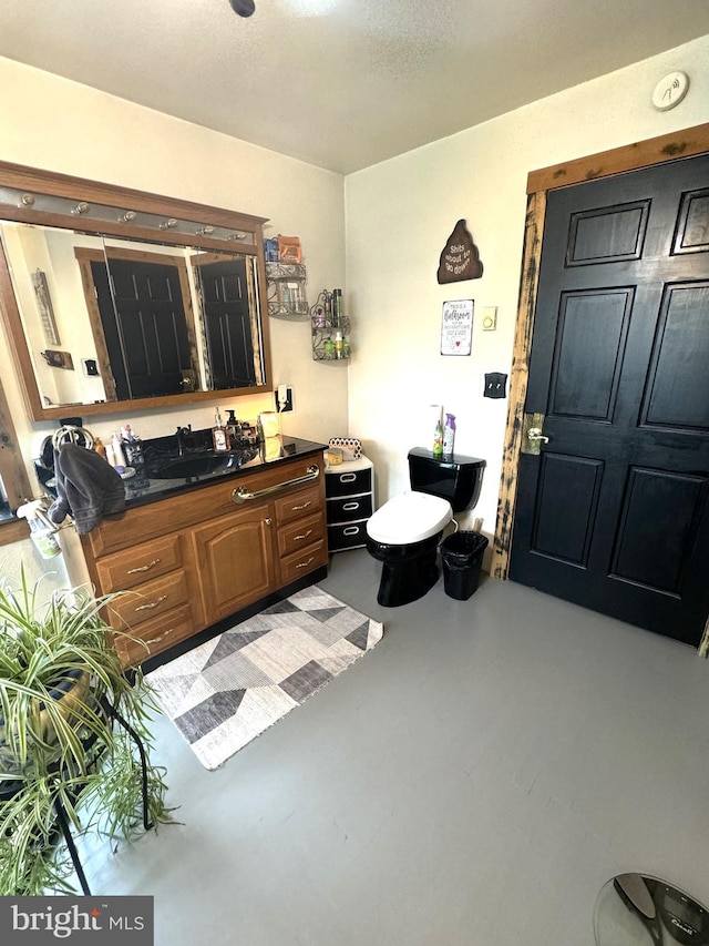 bathroom with a textured ceiling, vanity, toilet, and concrete flooring