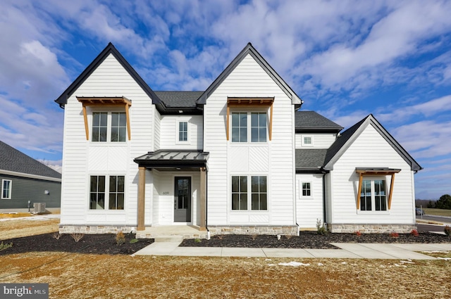 modern farmhouse featuring a standing seam roof, central AC unit, roof with shingles, and metal roof