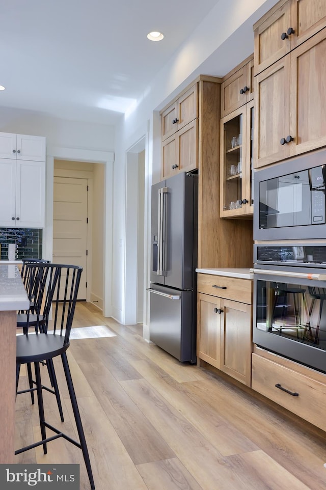 kitchen featuring built in microwave, light brown cabinets, light hardwood / wood-style floors, decorative backsplash, and high end fridge