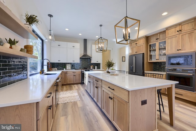 kitchen with a large island, sink, stainless steel appliances, wall chimney range hood, and a chandelier