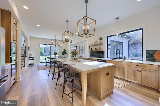 kitchen featuring a center island, sink, hanging light fixtures, light wood-type flooring, and stainless steel appliances