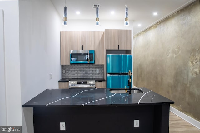 kitchen with pendant lighting, light hardwood / wood-style flooring, appliances with stainless steel finishes, light brown cabinets, and decorative backsplash