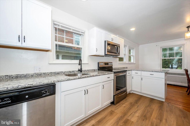 kitchen featuring stainless steel appliances, sink, hardwood / wood-style floors, radiator heating unit, and white cabinetry