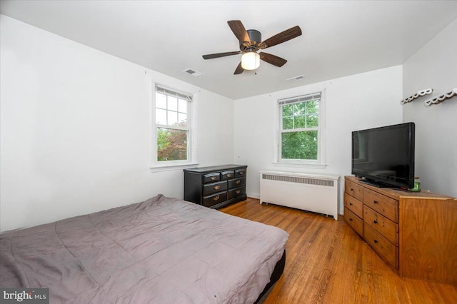 bedroom with multiple windows, light hardwood / wood-style floors, radiator, and ceiling fan