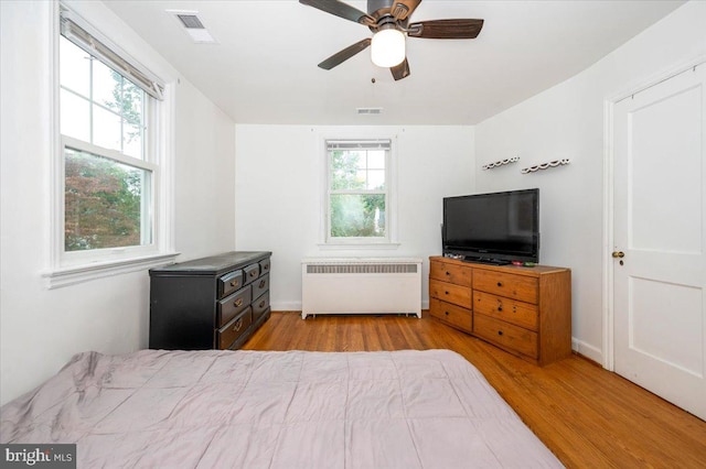 bedroom featuring radiator heating unit, light hardwood / wood-style floors, multiple windows, and ceiling fan