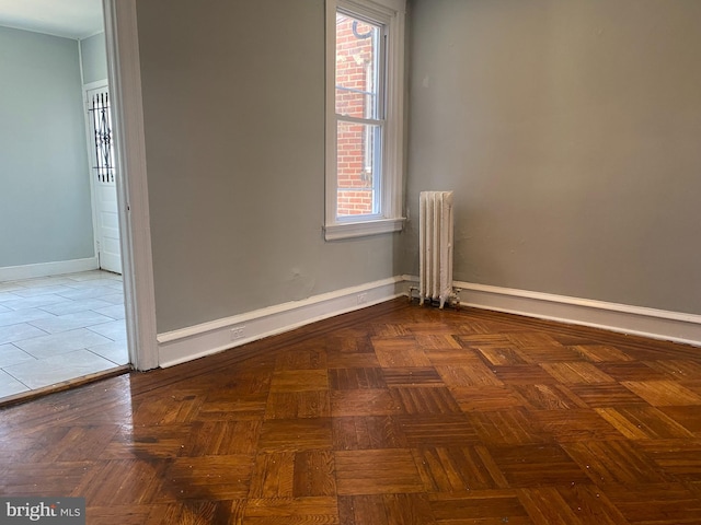 empty room featuring radiator heating unit, plenty of natural light, and dark parquet flooring