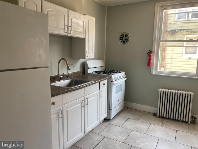 kitchen featuring white appliances, radiator, white cabinetry, and sink