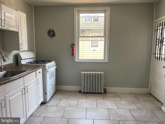 kitchen featuring white gas range, light tile patterned floors, radiator heating unit, sink, and white cabinets