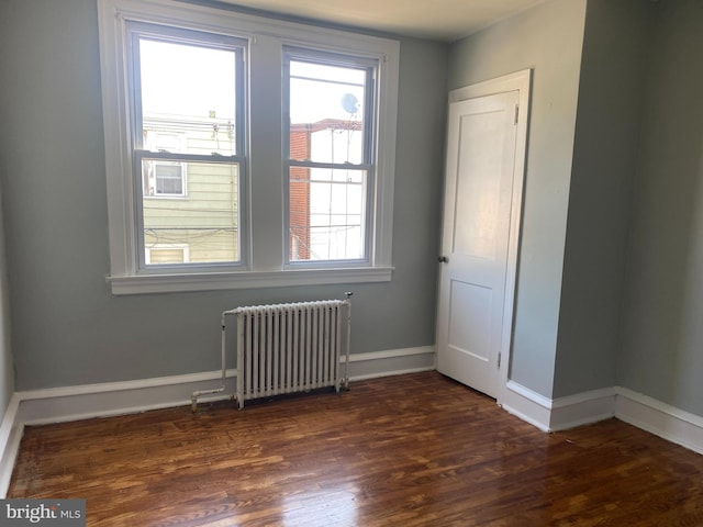 empty room with dark hardwood / wood-style floors, radiator heating unit, and a healthy amount of sunlight