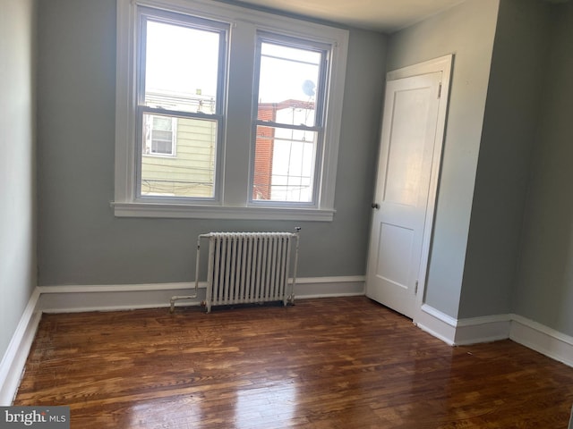 empty room featuring radiator heating unit and dark hardwood / wood-style flooring