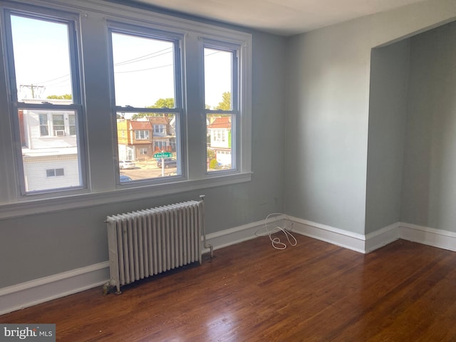 unfurnished room featuring dark hardwood / wood-style floors, radiator heating unit, and a healthy amount of sunlight