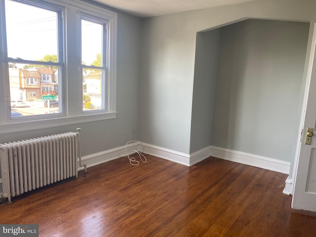 empty room with radiator, a wealth of natural light, and dark wood-type flooring