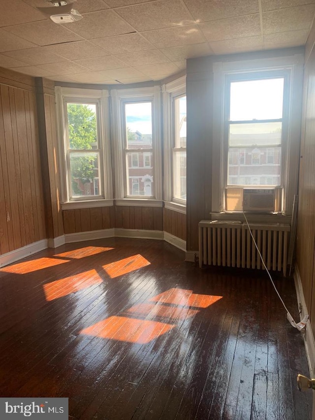 spare room featuring cooling unit, dark hardwood / wood-style floors, radiator heating unit, and wooden walls