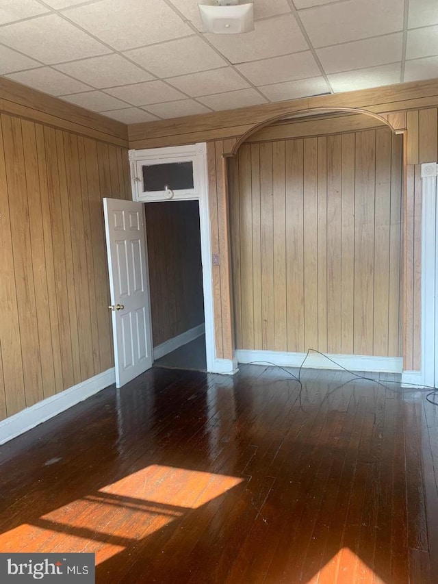 empty room with wood walls, wood-type flooring, and a drop ceiling