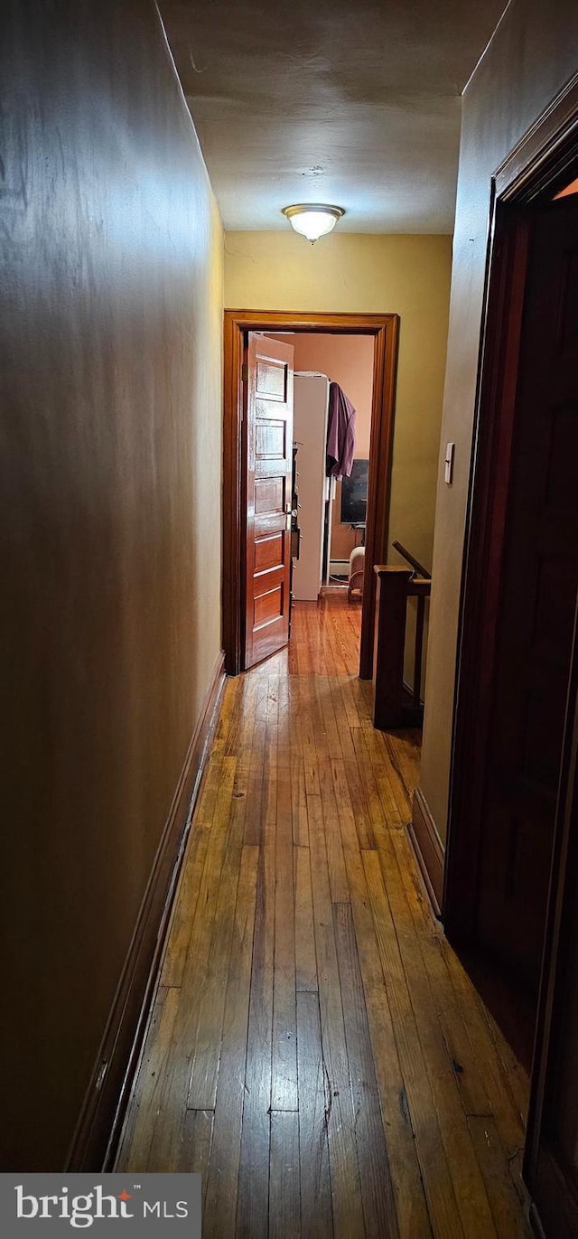 corridor featuring baseboards and dark wood-type flooring