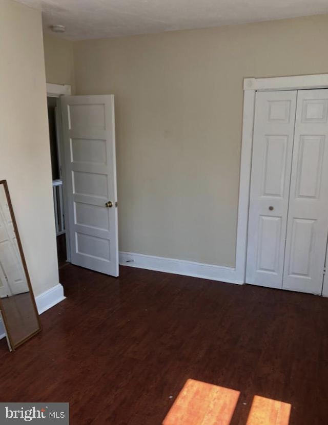 unfurnished bedroom with dark wood-type flooring and a closet