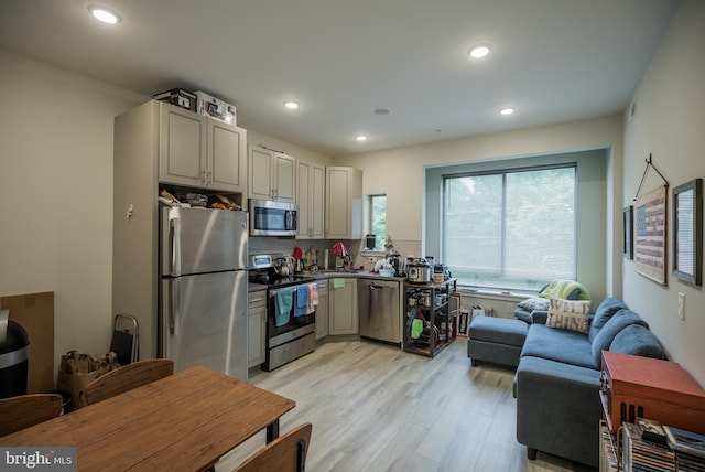 kitchen with appliances with stainless steel finishes, backsplash, light hardwood / wood-style floors, and gray cabinets