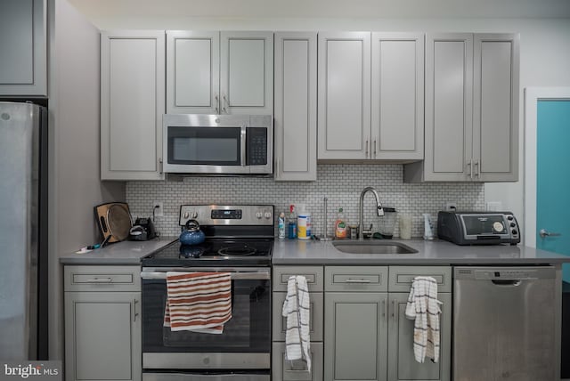 kitchen featuring gray cabinetry, decorative backsplash, appliances with stainless steel finishes, and sink