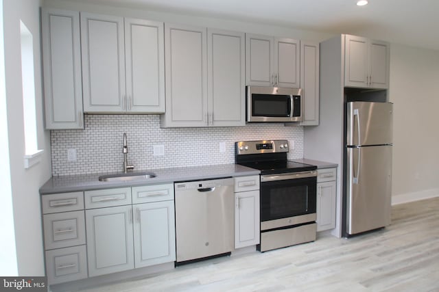 kitchen featuring sink, tasteful backsplash, gray cabinets, stainless steel appliances, and light wood-type flooring