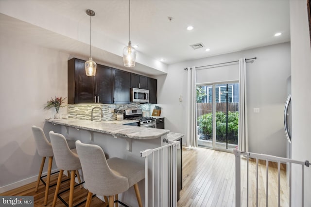 kitchen with a kitchen breakfast bar, light hardwood / wood-style floors, stainless steel appliances, decorative backsplash, and light stone counters