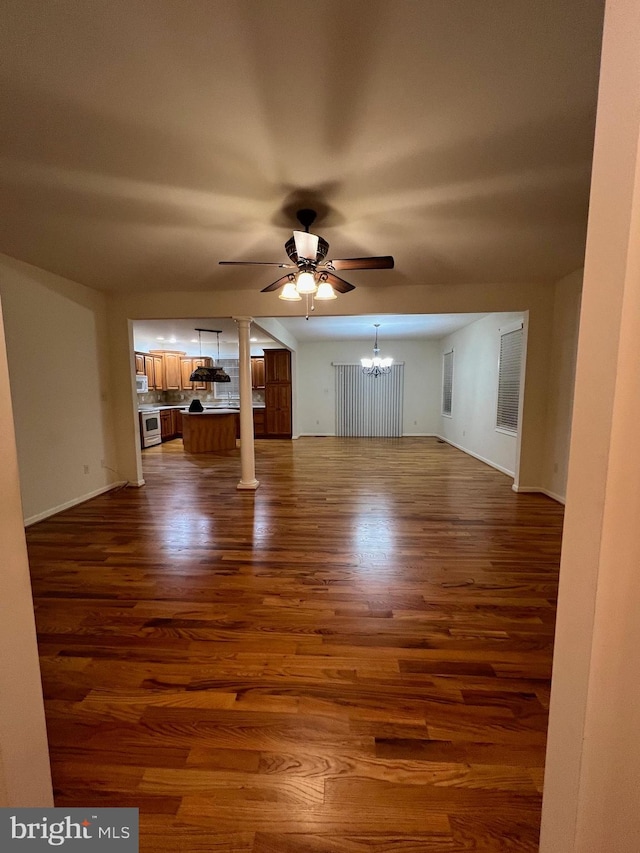 unfurnished living room featuring dark wood-type flooring, decorative columns, ceiling fan with notable chandelier, and baseboards