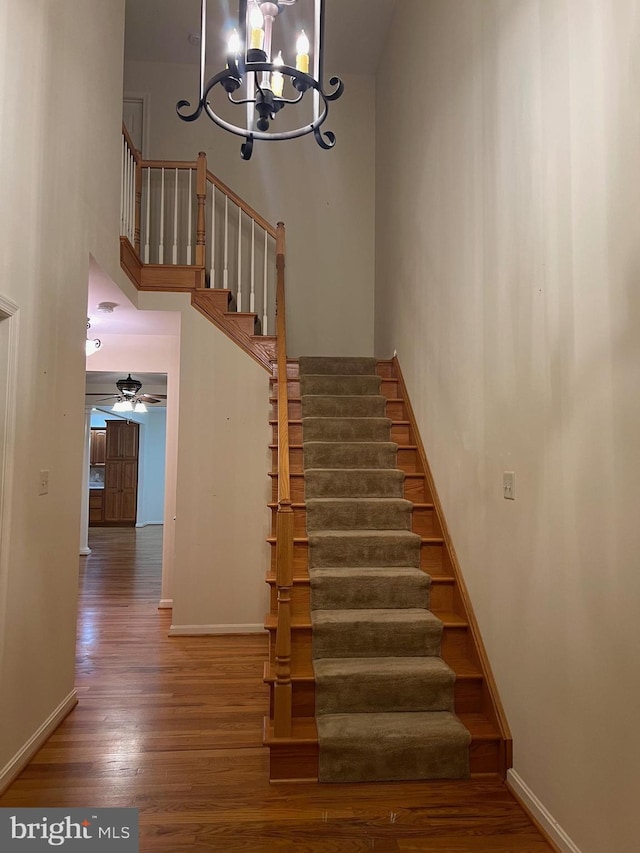 stairs with ceiling fan with notable chandelier, wood-type flooring, and a high ceiling