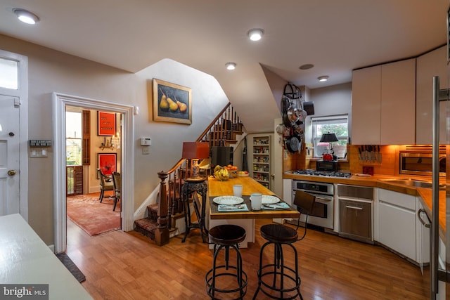 kitchen with backsplash, appliances with stainless steel finishes, white cabinetry, light hardwood / wood-style flooring, and sink