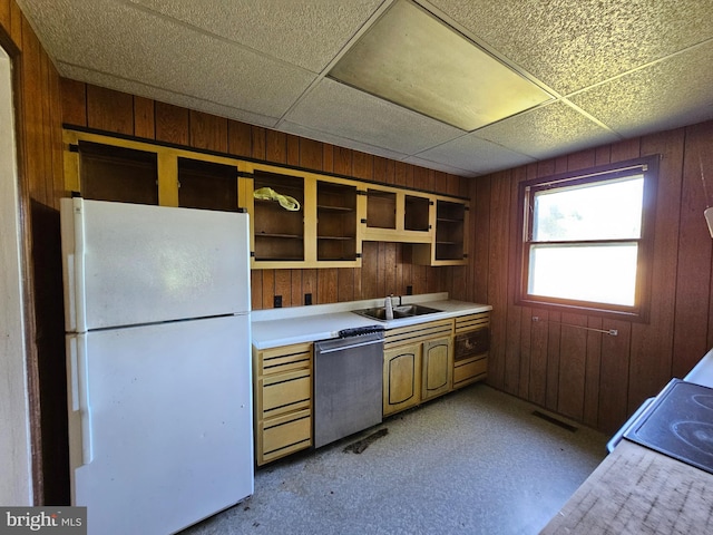 kitchen with sink, stainless steel dishwasher, white fridge, a paneled ceiling, and wood walls