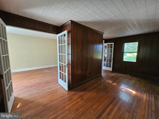 unfurnished room featuring french doors, a textured ceiling, wooden walls, and hardwood / wood-style floors